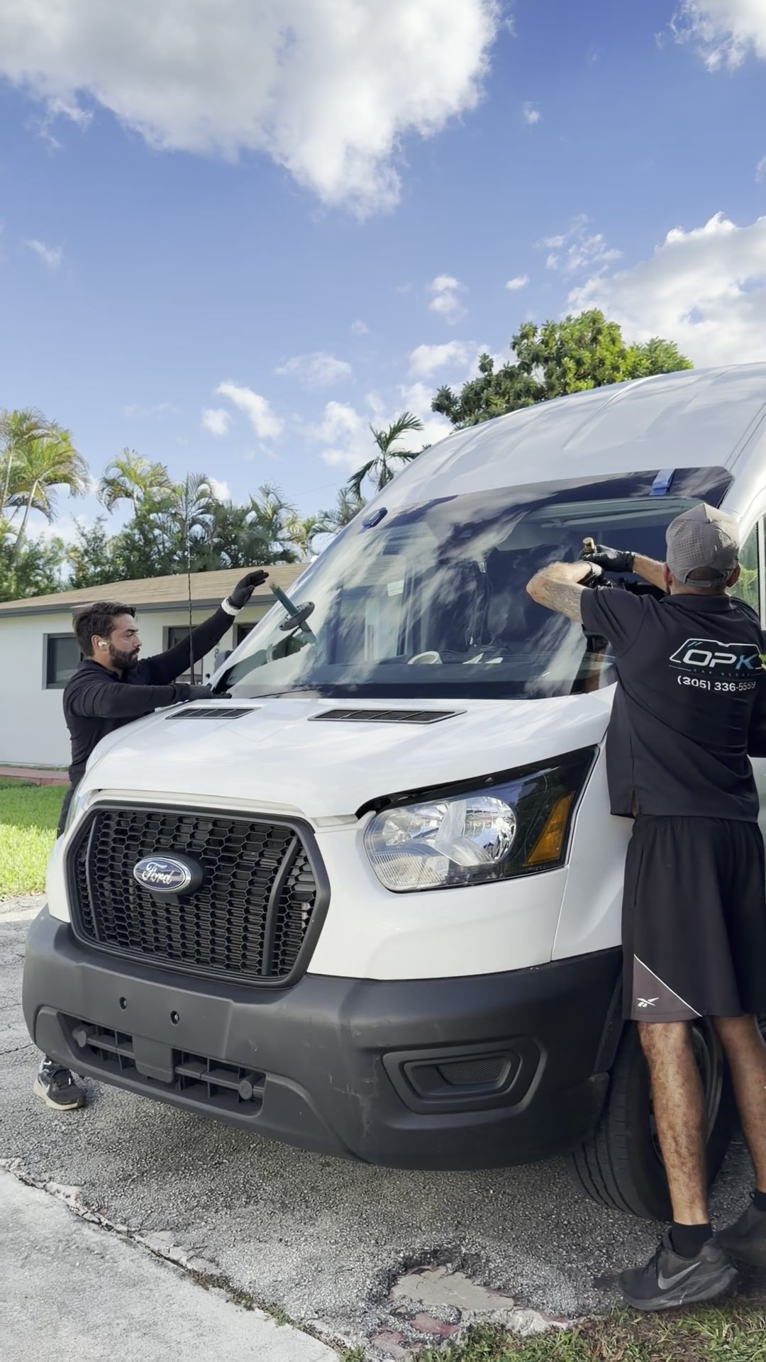 Two OPK technicians setting a new windshield on a Ford Transit van in a customer's driveway